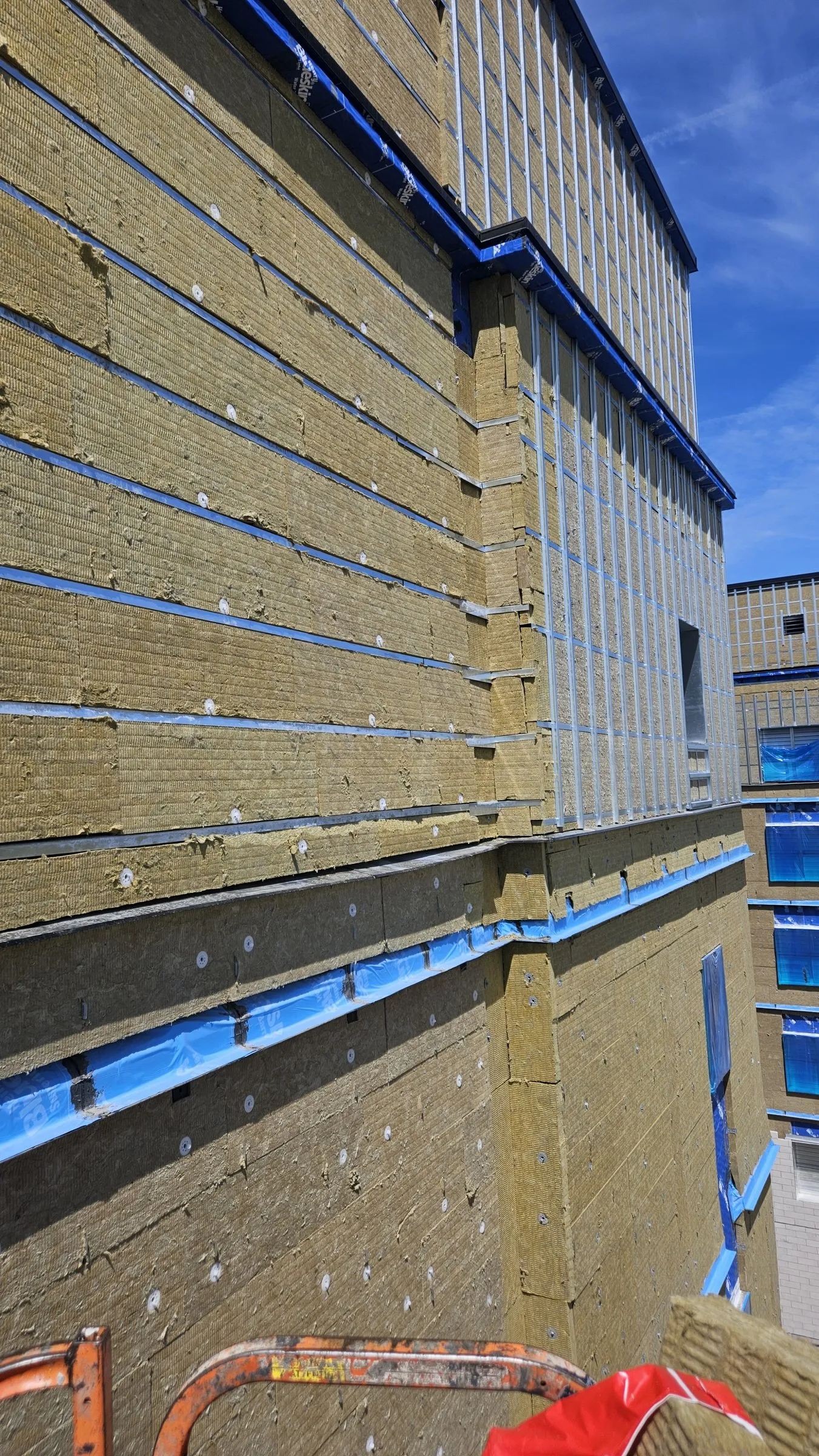 Mineral wool boards with fasteners and blue membrane flashings at floor lines