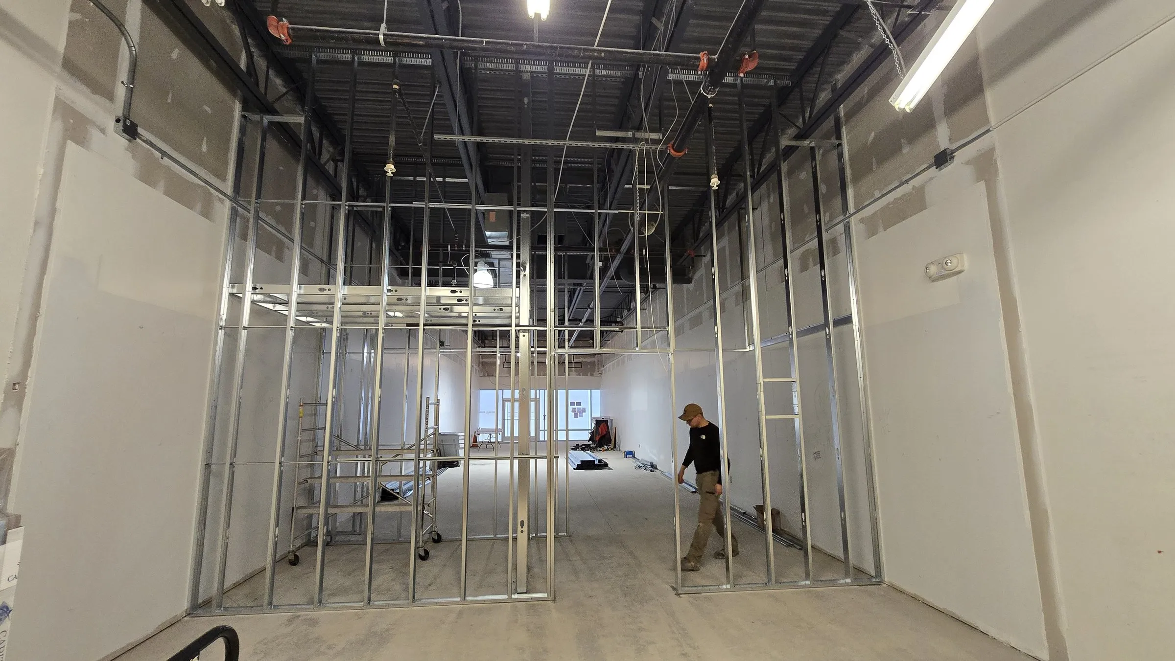 Full-height steel stud partitions in a tall open-plan unit, with a rolling scaffold and a framer on site