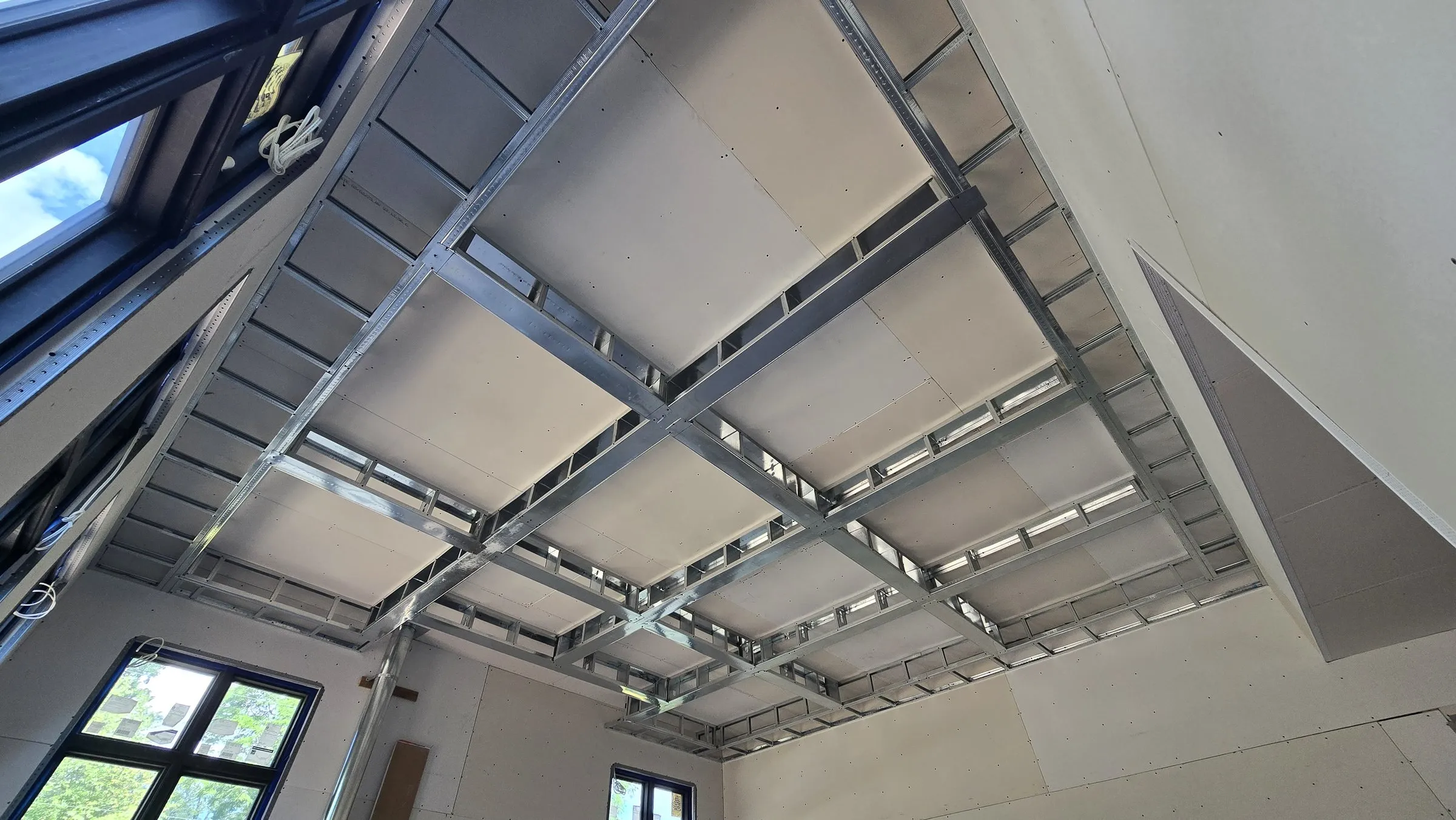 Steel ceiling framing following a sloped roof, first drywall boards installed