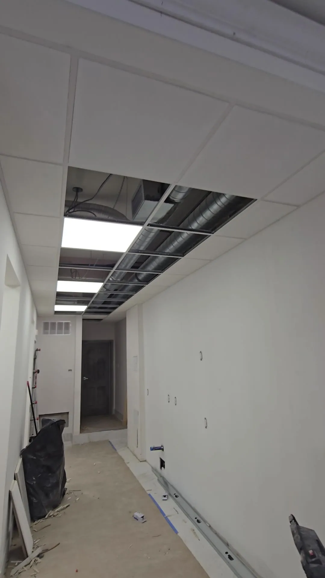 Video of a corridor with a T-bar ceiling grid and light panels, and finished drywall rooms