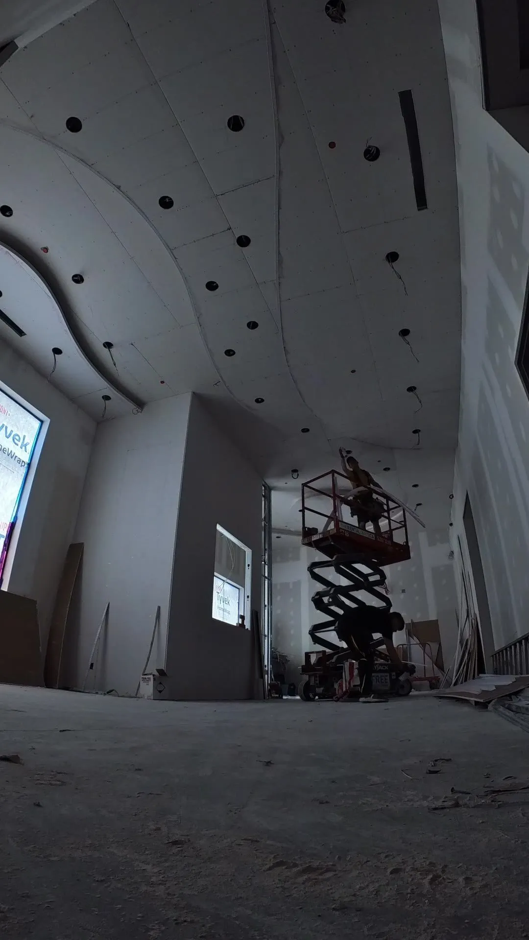 Time-lapse video of a curved drywall ceiling being boarded from scissor lifts in a triple-height hall